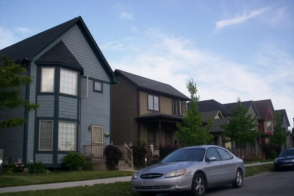 Two-storey houses with porches along a residential street, one painted blue, with mature planting