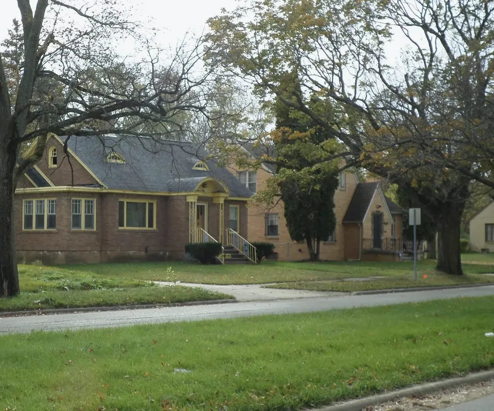 Brick houses with bracketed entry hoods and eyebrow dormers along a street of mature trees and mown lawns