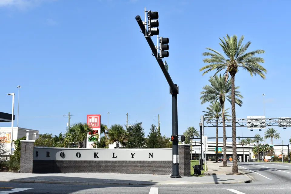 A street-level neighbourhood marker reading BROOKLYN beside a road in Jacksonville, Florida, with palm trees and an interstate overpass behind it.
