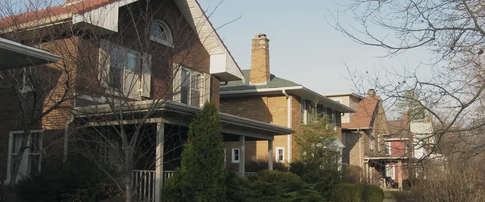 A two-storey house with a full-width front porch and established planting on a residential street