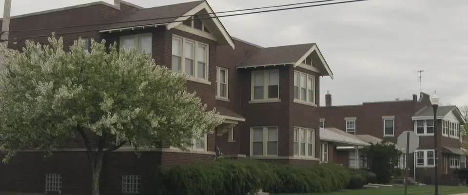 A modest two-unit residential building seen from the pavement, with no people in frame