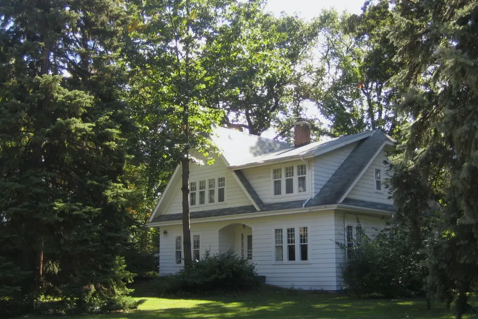 A modest post-war house with a covered porch, front lawn and established shrubs